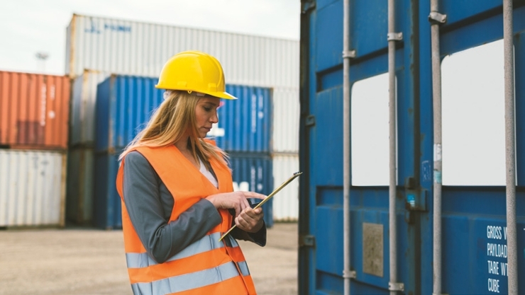 © iStock | vgajic A woman wears a hard hat and looks at a clipboard.