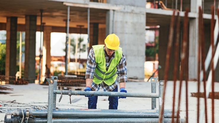 © iStock | Drazen A construction worker lifting heavy scaffolding parts