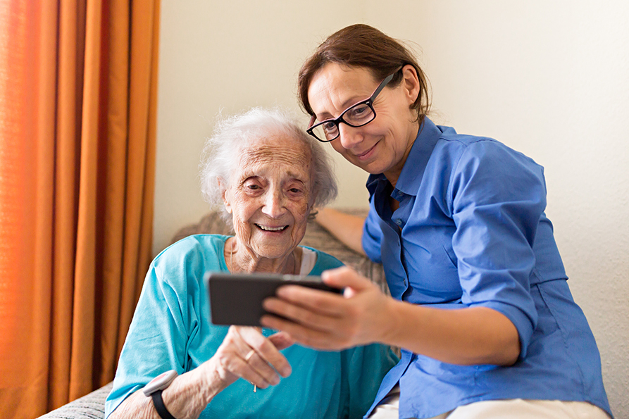 Altenpflegerin betrachtet mit Seniorin ein Smartphone