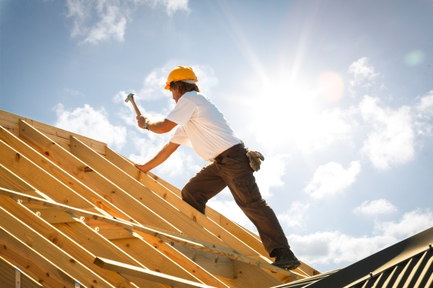 Arbeiter auf einem Hausdach, einen Zimmermannshammer in der linken Hand haltend