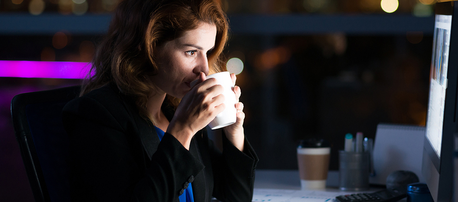 Frau sitzt mit Kaffeetasse in dunkler Umgebung vor einem Computer.