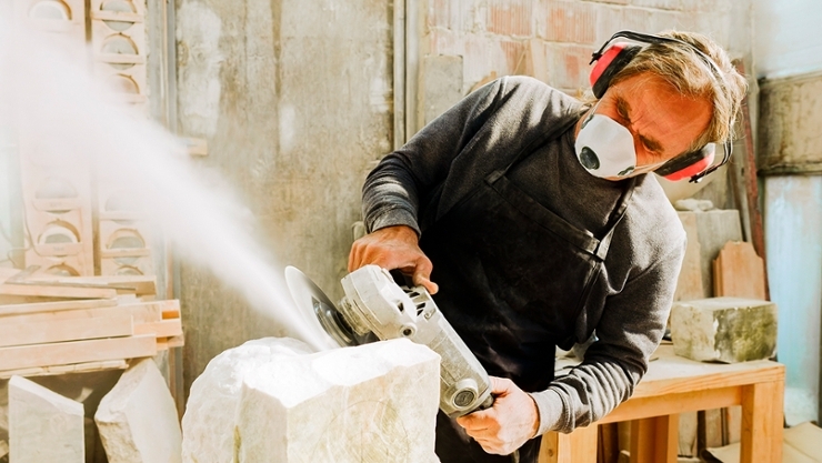 The photo shows a stonemason working with a grinder that produces a lot of dust.